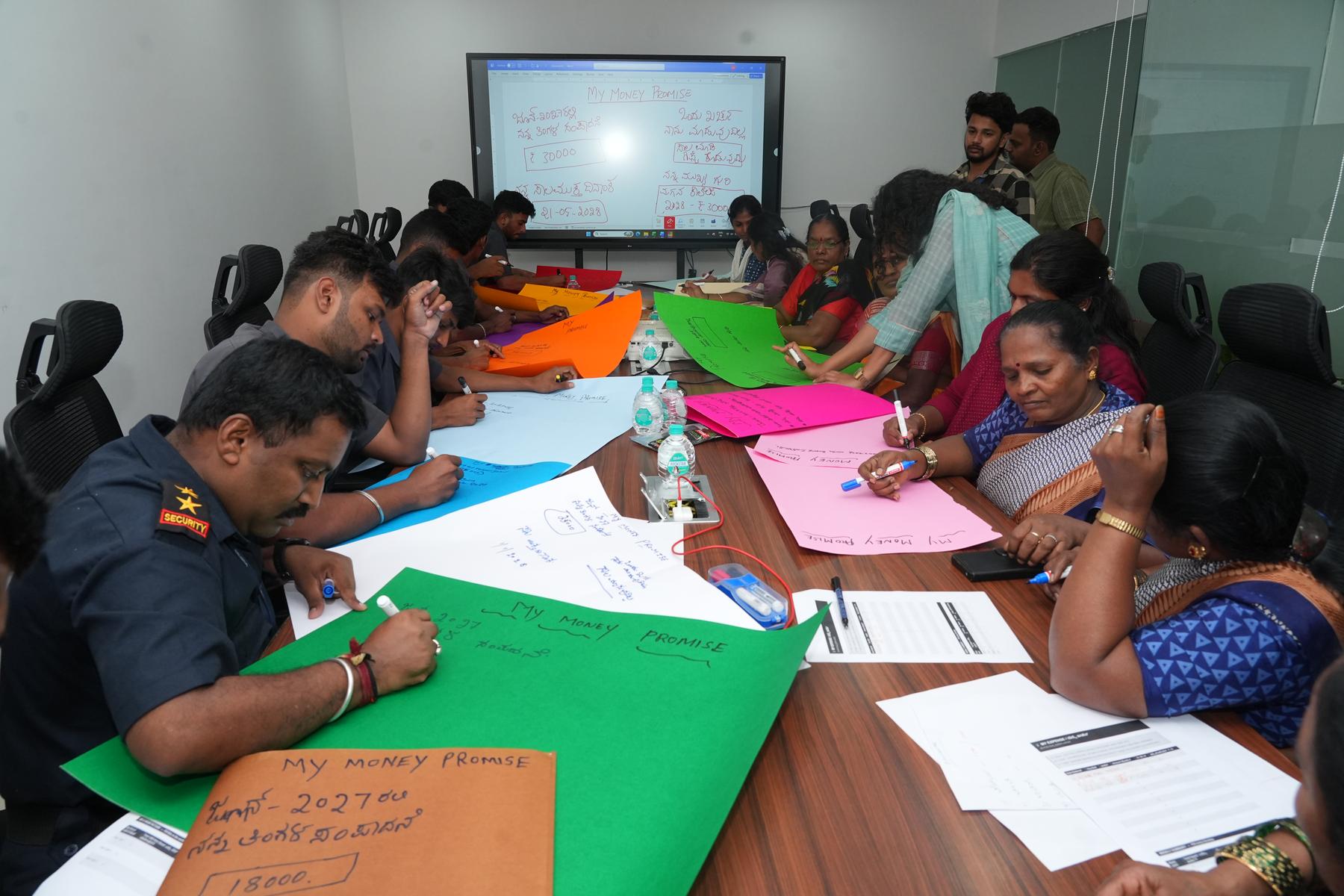 Participants actively writing their My Money Promise on colourful paper during a financial empowerment training